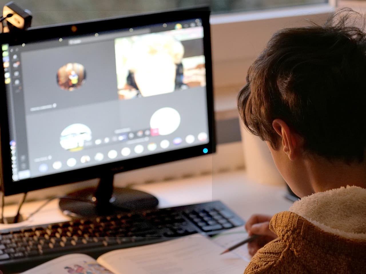 A child following an online class at a desk, taking notes in an exercise book